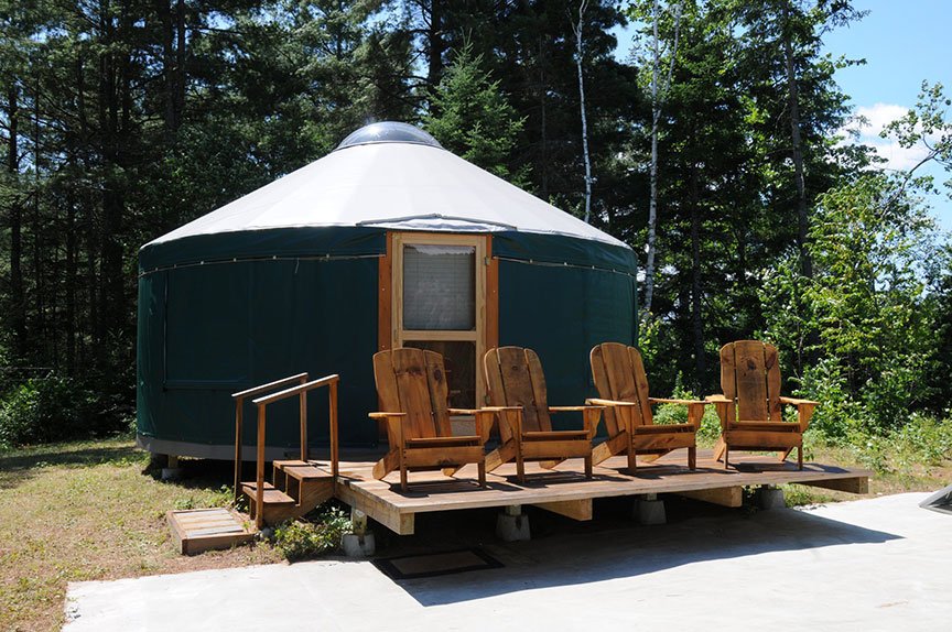 A 20 foot yurt with a wooden deck and chairs in the woods